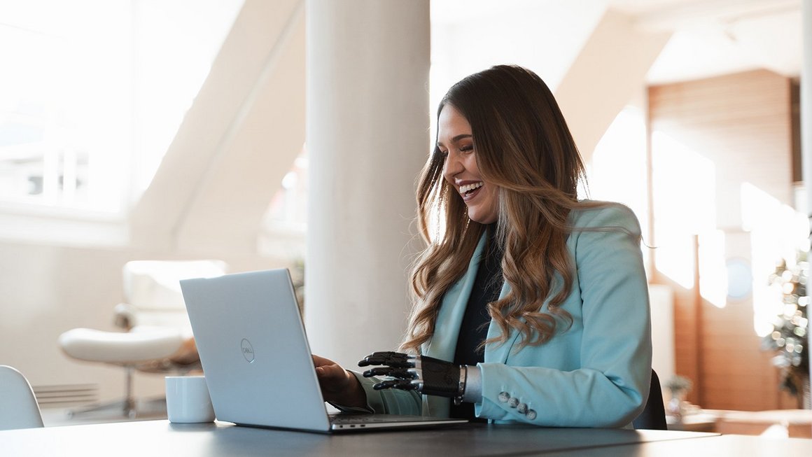 Produktivität am Arbeitsplatz steigern: 10 Tipps für produktives Arbeiten Frau arbeitet produktiv am Laptop und lacht